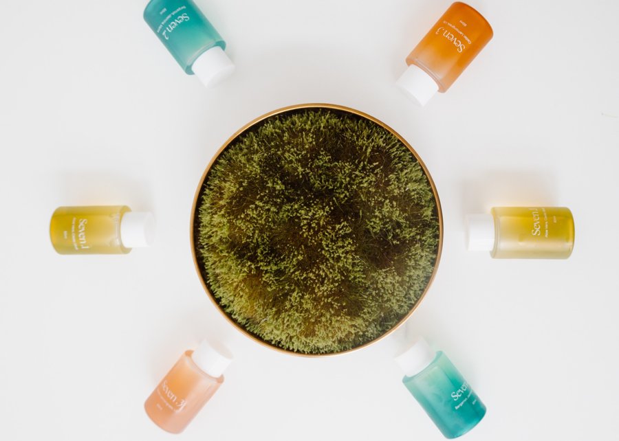 A flat lay of colorful skincare containers around a bowl of moss