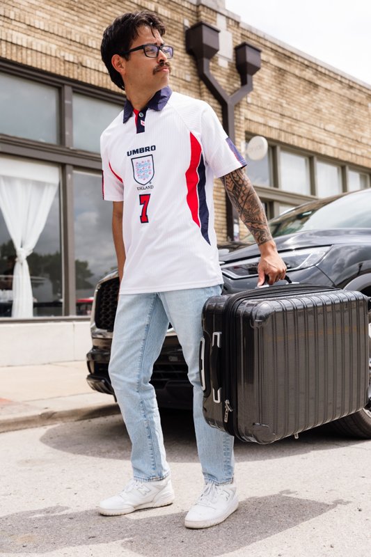 A model standing beside a black suitcase on a city sidewalk