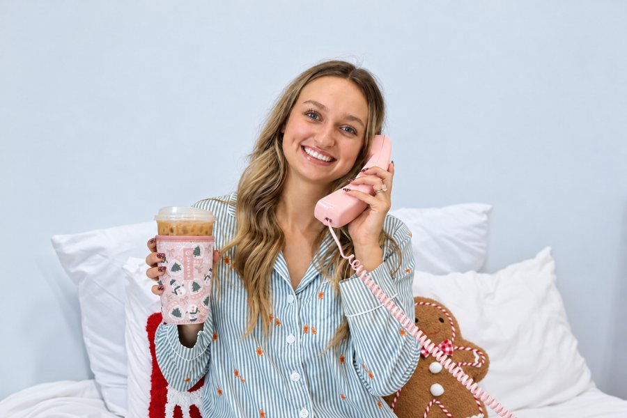 A smiling model holding a pink telephone and an iced drink in a patterned sleeve