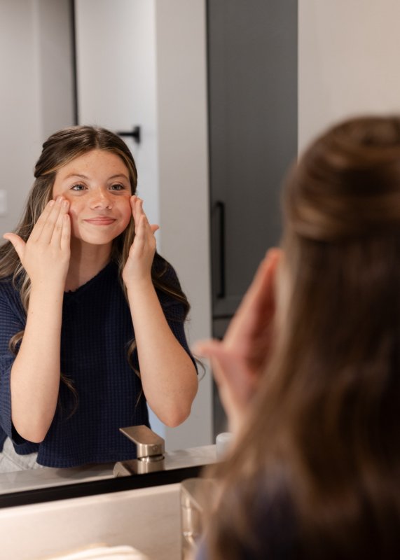 A person applying skincare at a mirror