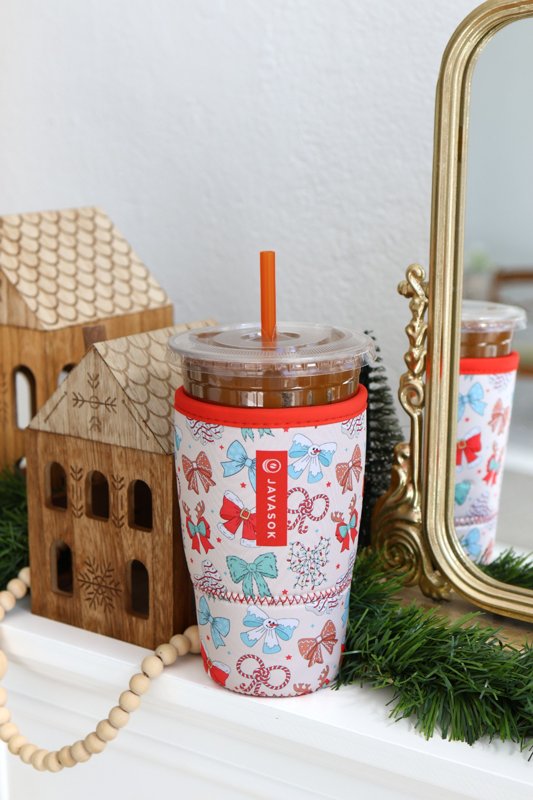 An iced drink in a patterned JavaSok sleeve beside a mirror and holiday decor